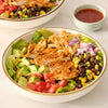A close-up of a delicious-looking chicken salad in a white bowl, featuring chicken seasoned with Mccormick Smoked Paprika And Garlic Seasoning, 3.12 Oz, alongside fresh lettuce, avocado, and beans.