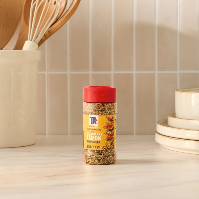 A bottle of Mccormick Rosemary Lemon Seasoning, 2.75 Oz sits on a kitchen counter, ready to be used in a recipe, with kitchen utensils and plates visible in the background.