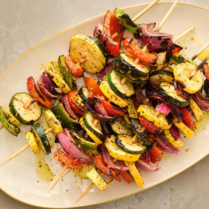 A close-up, overhead view of grilled vegetable skewers, featuring zucchini, red onion, and bell peppers, seasoned with Mccormick Rosemary Lemon Seasoning, 2.75 Oz and arranged on a white platter.