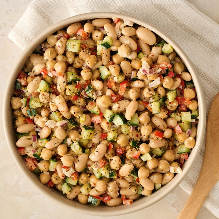 A fresh bean salad with chickpeas and diced vegetables is presented in a bowl, showcasing a recipe made with Mccormick Rosemary Lemon Seasoning, 2.75 Oz.