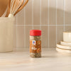A bottle of Mccormick Sesame Ginger Seasoning, 2.5 Oz, is placed on a light-colored kitchen countertop, with kitchen utensils and plates in the background.