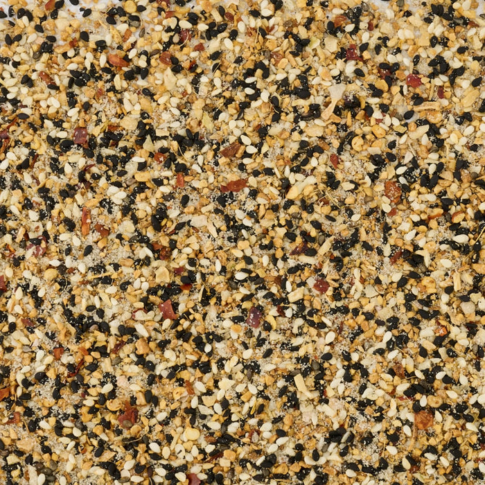 An overhead, close-up view displays the texture and ingredients of Mccormick Sesame Ginger Seasoning, 2.5 Oz, including black and white sesame seeds, and dried garlic.