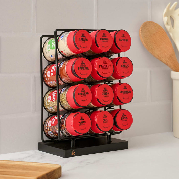 A Mccormick Spice Rack Red Cap Black Metal 12 Ct is displayed on a kitchen counter, featuring red-capped jars of various McCormick spices like garlic salt, cumin, paprika, thyme, oregano, and cinnamon.