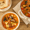 A hearty bowl of seafood stew, a perfect dish to create using a seasoning like Mccormick, 10.49 Oz, is served on a wooden table with crusty bread.