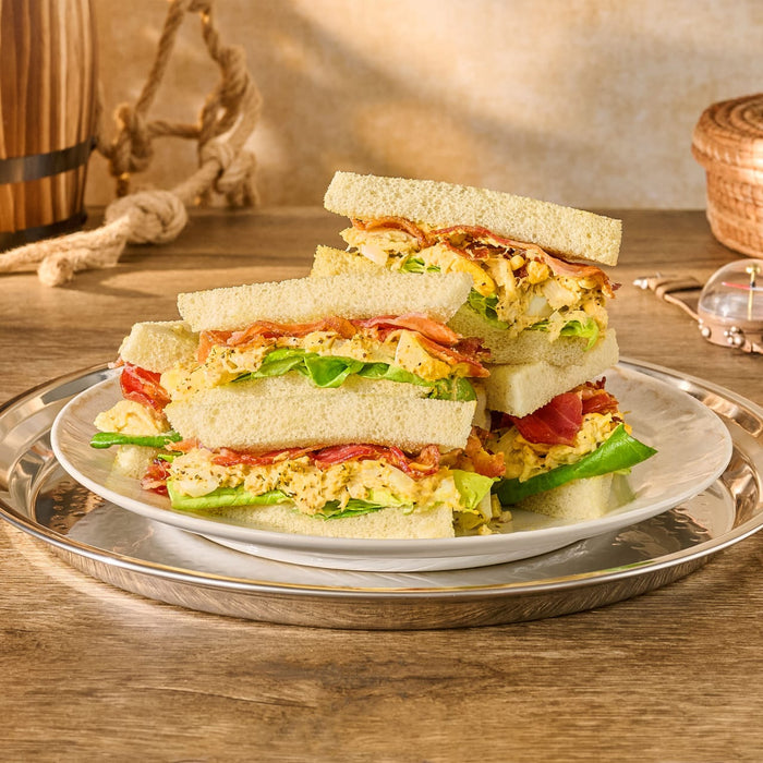 A stack of crustless club sandwiches filled with a creamy salad, bacon, and lettuce sits on a silver platter, showing a delicious recipe idea using a seasoning like Mccormick, 10.49 Oz.