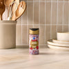 A bottle of Mc Mixed Berry Fin Sgr 72/6/3.15 Oz is centered on a light-colored kitchen countertop, with a utensil crock and stacked plates in the background to create a pleasant culinary scene.