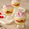 Three individual glass cups of raspberry trifle are arranged on a tray, each topped with whipped cream and a festive garnish of Mc Mixed Berry Fin Sgr 72/6/3.15 Oz.