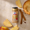 A bottle of Mccormick Apple Pie Finishing Sugar, 3.06 Oz, is arranged on a light-colored surface with fresh apple slices, cinnamon sticks, and a golden-brown apple pie.
