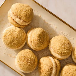 A top-down view shows several golden sandwich cookies with a cream filling, beautifully arranged on a platter and sprinkled with Mccormick Apple Pie Finishing Sugar, 3.06 Oz.