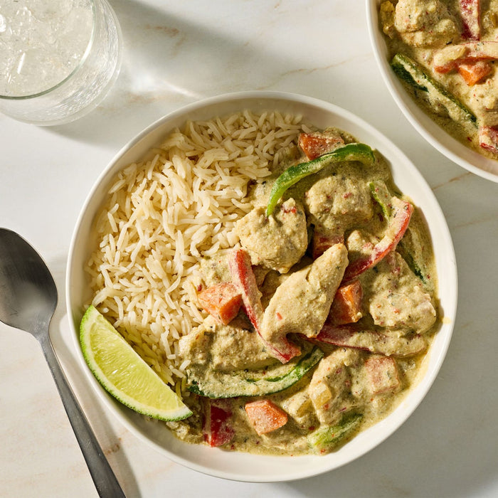 A bowl of creamy green curry with chicken and vegetables served alongside white rice and a lime wedge is prepared using Mc Thai Gn Curry Mix.