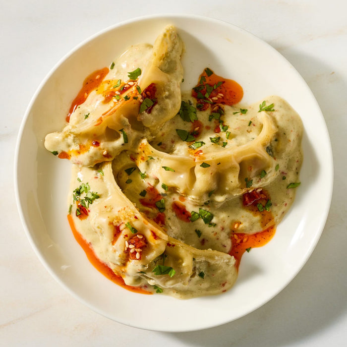 A white plate holds three large dumplings smothered in a creamy sauce made with Mc Thai Gn Curry Mix and finished with a drizzle of chili oil and fresh herbs.
