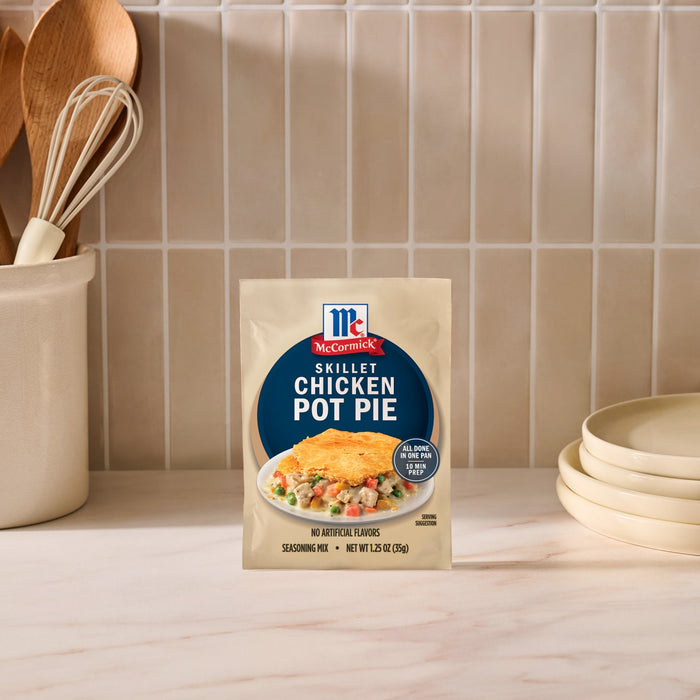 A package of Mc Chkn Pot Pie Mix stands on a marble countertop in a kitchen setting with wooden utensils and stacked plates.