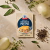 A package of Mc Chkn Pot Pie Mix is surrounded by fresh ingredients like onions, sage, thyme, and black peppercorns on a neutral stone surface.