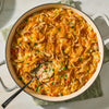 A large white skillet filled with a creamy chicken pot pie casserole made using Mc Chkn Pot Pie Mix and topped with melted cheddar cheese and crispy fried onions.