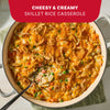 A large skillet filled with a cheesy and creamy rice casserole featuring peas and carrots topped with melted cheddar and crispy fried onions made using Mc Chkn Pot Pie Mix.