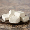 A stack of homemade marshmallows dusted with powdered sugar sits on a brown plate.