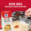 A box of McCormick Vanilla Flavor is shown as a tablespoon of vanilla extract is being poured into pancake or muffin batter.
