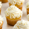 A close-up of several cupcakes with white frosting arranged on a light surface.