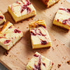 Several pieces of raspberry swirl cheesecake are arranged on a wooden cutting board showcasing a delicious dessert.