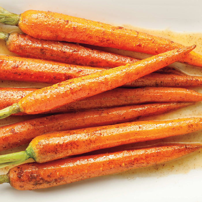 A vibrant pile of glazed carrots with fresh green tops.