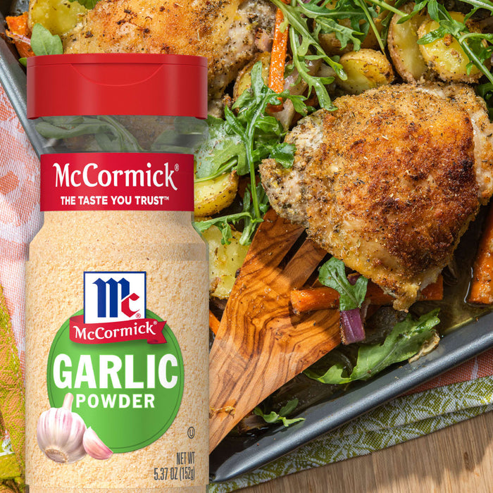 A bottle of McCormick Garlic Powder next to a baking dish of roasted chicken potatoes carrots and arugula.