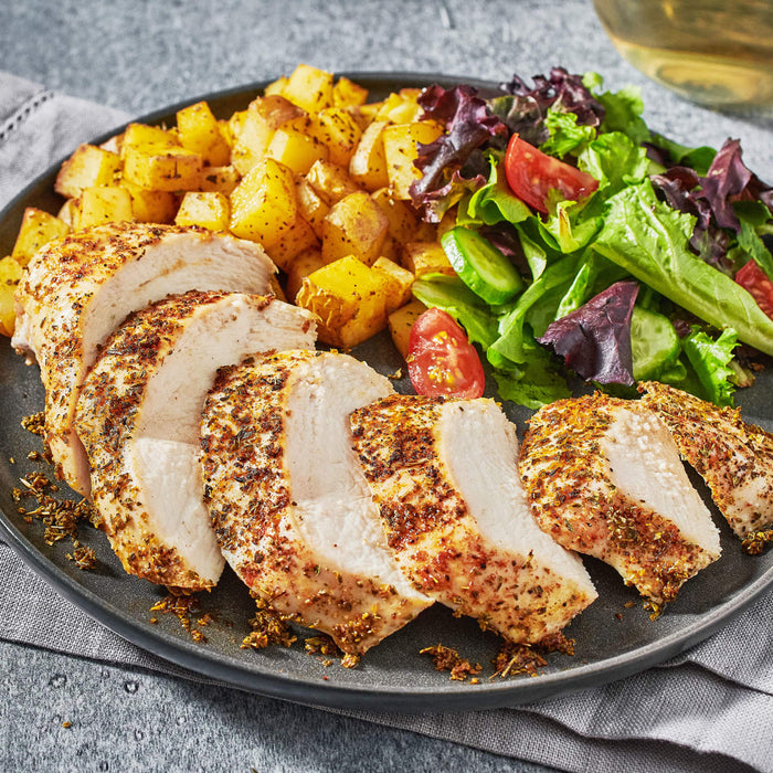 A plate of sliced chicken breast with roasted potatoes and a side salad.