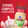 A jar of McCormick Garlic Powder with fresh garlic cloves around it.
