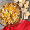 ['A casserole dish filled with a cheesy, meaty dish topped with pickles and onions, with toasted bread on the side.']