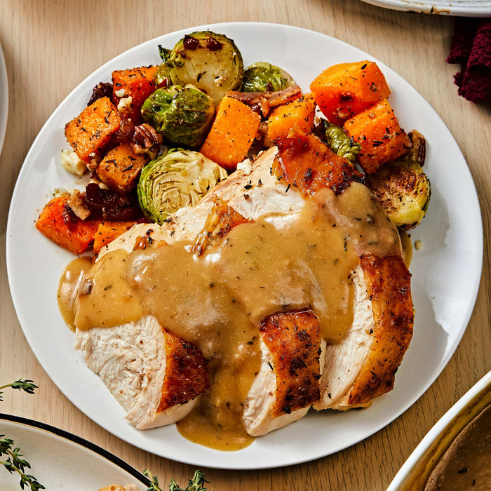 ['A plate of roasted turkey with gravy, Brussels sprouts, and butternut squash.']