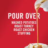 ['A white bowl pours gravy over mashed potatoes, roast turkey, roast chicken, and stuffing.']
