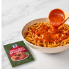 A bowl of spaghetti with McCormick Thick &amp; Zesty Spaghetti sauce being poured over it.