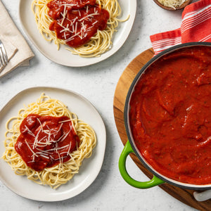 A pot of red sauce sits on a wooden cutting board with a red and white striped towel next to it.