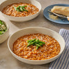 Two bowls of risotto with parmesan cheese and two forks on a white surface.
