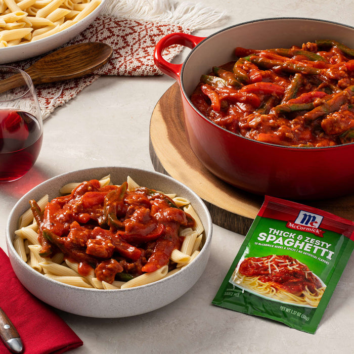 ['A bowl of pasta with a red sauce and green peppers, a red pot with the same pasta and sauce, and a McCormick Thick &amp; Zesty Spaghetti packet.']