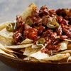 ['A bowl of nachos topped with chili, jalapenos, and cheese.']