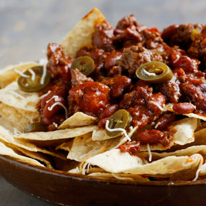 ['A bowl of nachos topped with chili, jalapenos, and cheese.']