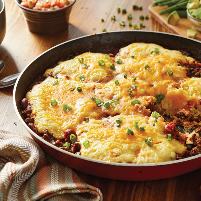 ['A skillet of cheesy cornbread topped with green onions.']