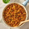 A skillet of chili cornbread casserole, made flavorful with Mccormick Chili Seasoning Mix 1.25 Oz, topped with melted cheese and green onions, with a portion scooped out, and salsa and avocado in the background.