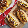 ['Three hot dogs topped with chili, onions, and mustard on a wooden cutting board.']