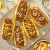Three chili dogs topped with mustard and onions, served alongside chili cheese waffle fries, are displayed, prepared with the flavorful Mccormick Chili Seasoning Mix 1.25 Oz.