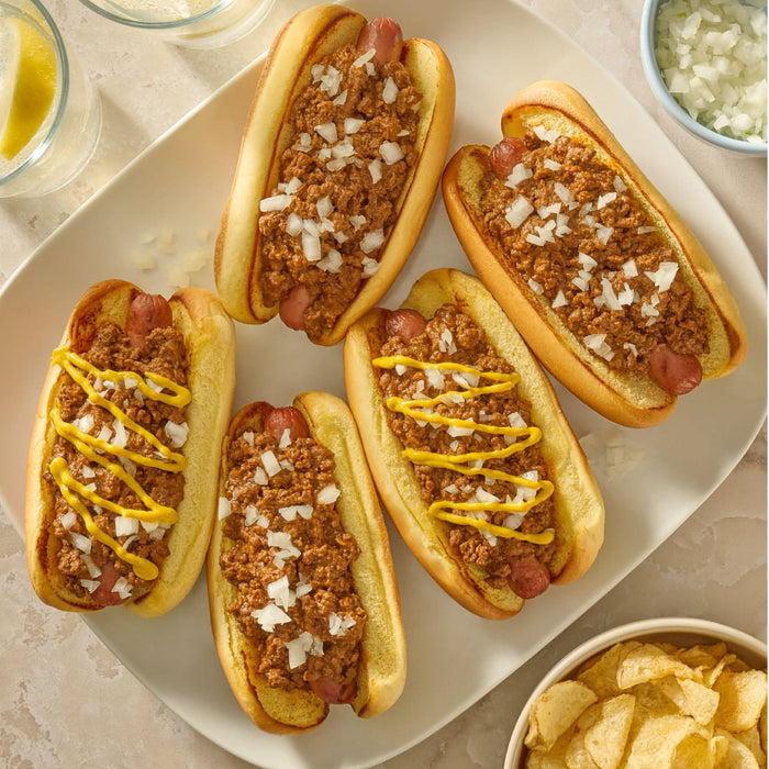 Three chili dogs topped with mustard and onions, served alongside chili cheese waffle fries, are displayed, prepared with the flavorful Mccormick Chili Seasoning Mix 1.25 Oz.