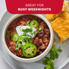 A pot of baked beans garnished with cheese and green onions is shown on a red background, illustrating the versatility of Mccormick Chili Seasoning Mix 1.25 Oz for dishes like baked beans, burgers, and dips.