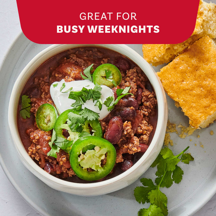 A pot of baked beans garnished with cheese and green onions is shown on a red background, illustrating the versatility of Mccormick Chili Seasoning Mix 1.25 Oz for dishes like baked beans, burgers, and dips.