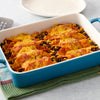 ['A blue baking dish filled with enchiladas topped with cheese and sauce.']
