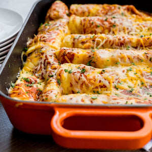 ['A close-up of a casserole dish filled with enchiladas topped with cheese and parsley.']