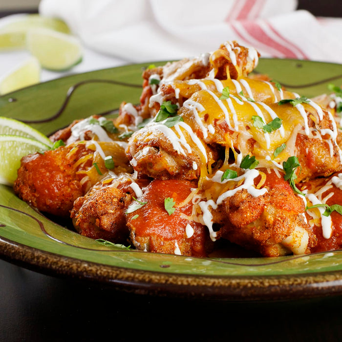 ['A plate of chicken wings covered in cheese, sour cream, and cilantro.']