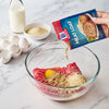A hand pours McCormick Meat Loaf seasoning mix into a bowl with ground beef bread crumbs and an egg.