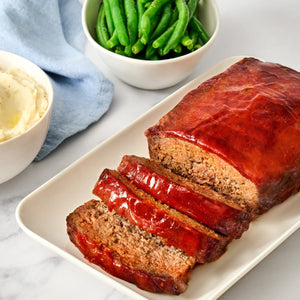 A white plate with a sliced meatloaf topped with a red sauce.