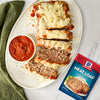 A plate of sliced meatloaf topped with marinara sauce and mozzarella cheese with a McCormick Meatloaf seasoning packet.