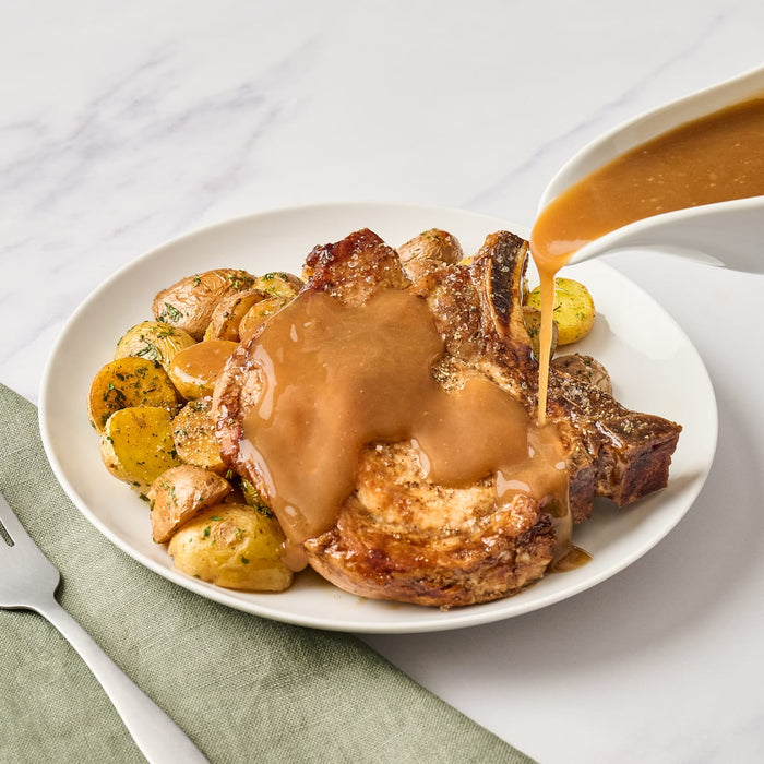 A plate of pork chops and potatoes with gravy being poured over them.